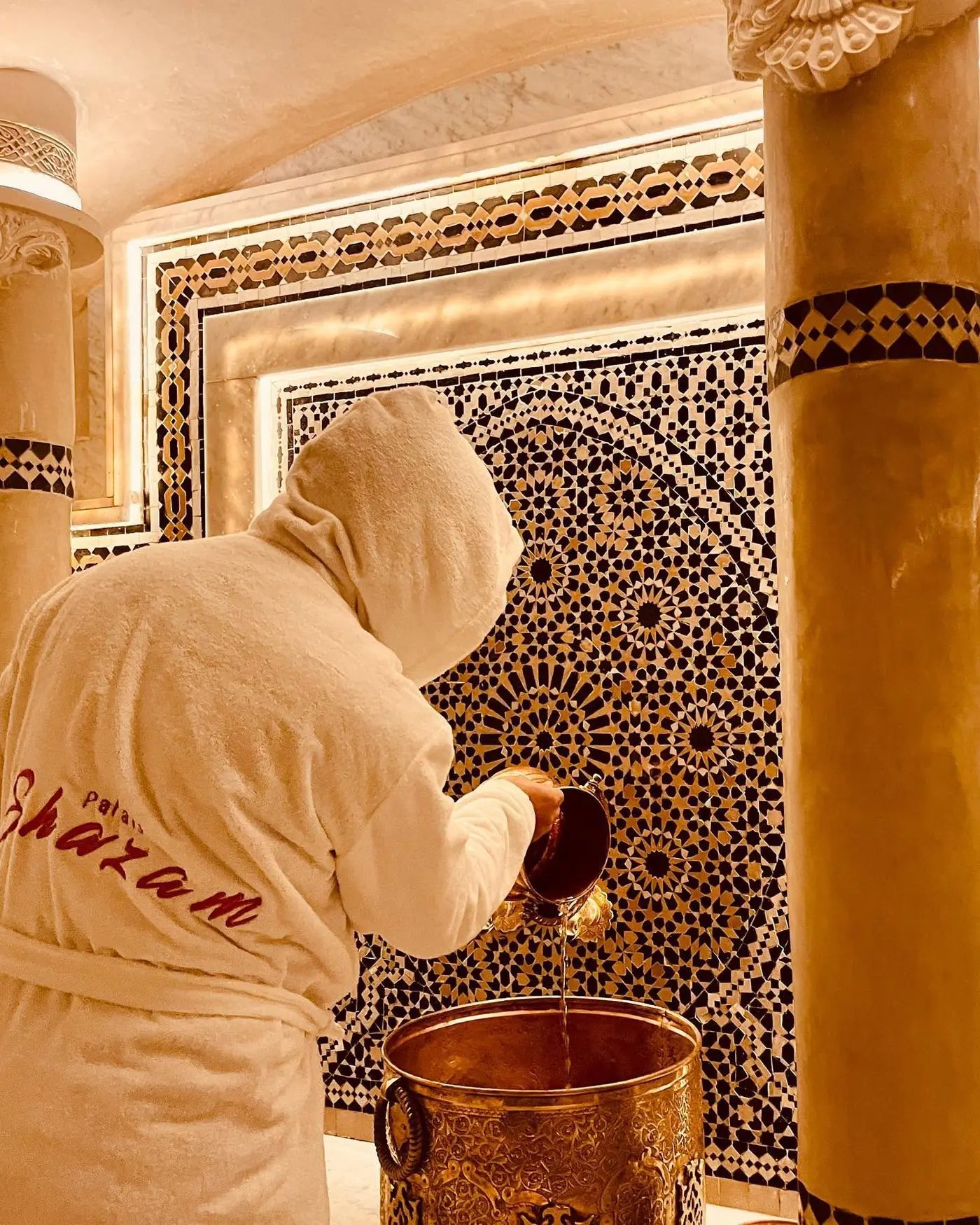 A guest in a Palais Shazam robe pouring water at the hammam's mosaic fountain